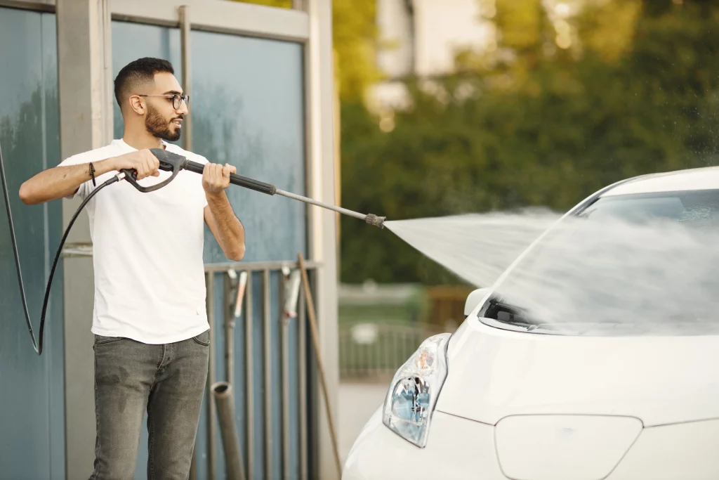 Homem usando uma lavadora de alta pressão para limpar o exterior de um carro.
